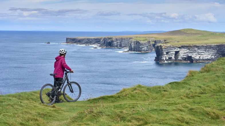 A woman cycling along the cliffs of Dunmore Head during summer in Ireland.