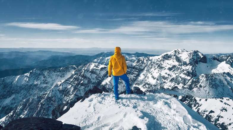 A man standing at the snow-covered top of the peak of Jebel Toubkal during winter in Morocco.