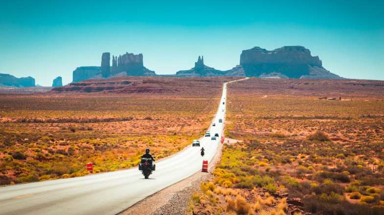 Travelers on the road in motorbikes and cars on the Route 66 highway during the day.