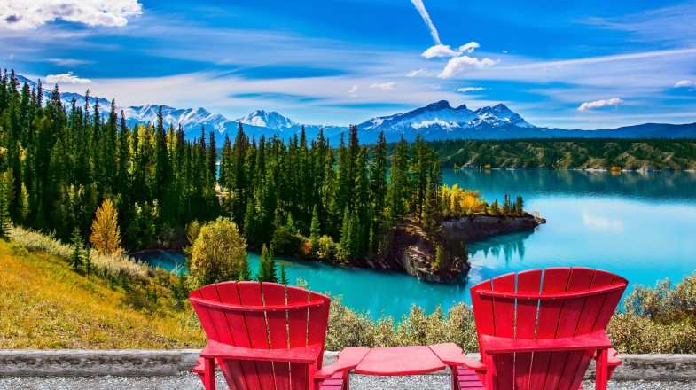 Two red loungers by the Abraham lake overlooking the trees and the mountains in Canada in September.