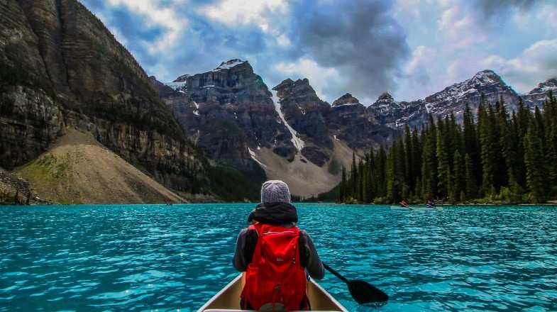 A traveler paddling on a boat on blue water during the day with mountains all around.