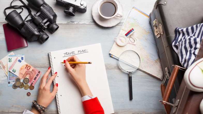 A woman listing out things to do on her notebook on her desk planning her trip.