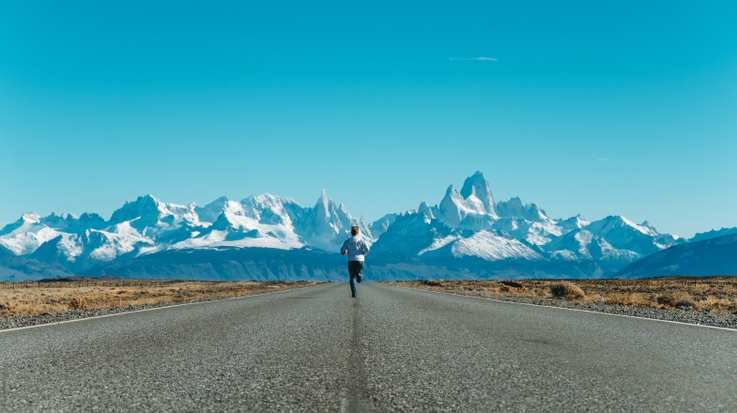 Man running on asphalt road toward snow-covered mountains in the background in Argentinian Patagonia on an Argentina itinerary.