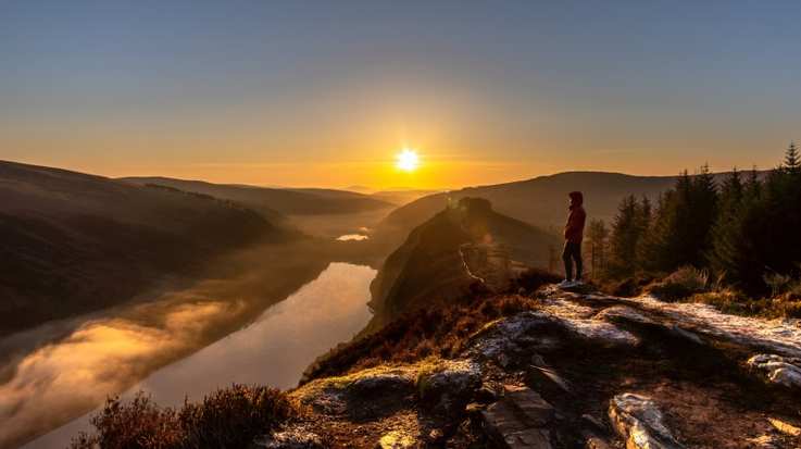 Man in orange jacket admiring the sunrise in Ireland in May.
