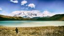 A trekker stands on a lakeshore and admires view of snow-covered mountain in Chile