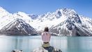 A girl sits on a rock overlooking a blue lake and snow-capped mountains in Cajon del Maipo during a 10-day Chile itinerary