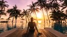 A woman sitting on a deck in an Indonesian resort looking at the sunset
