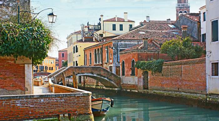 The leisure walk through the narrow streets of Dorsoduro neighborhood with tiny bridges tilted colorful villas and quiet canals in Venice.