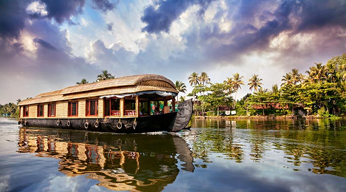 House boat in backwaters near palms at cloudy blue sky in Alappuzha Kerala India
