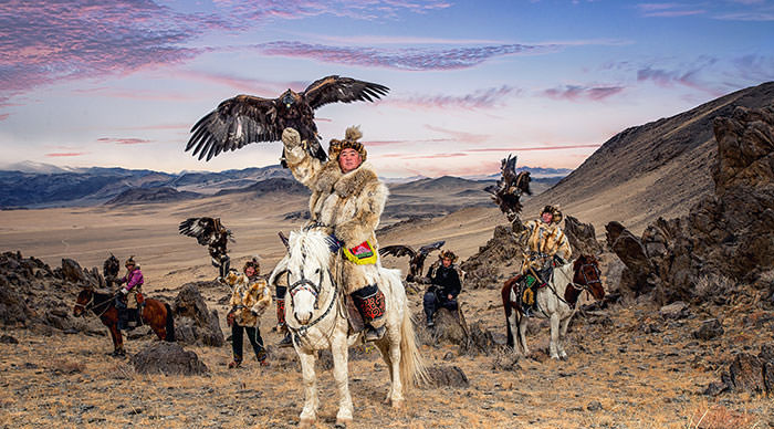 Kazakh Eagle Hunter in traditionally trained golden eagles riding horse in Mongolia